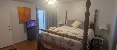 A bedroom with a four-poster bed, a ceiling fan, a television, and a nightstand with a lamp.