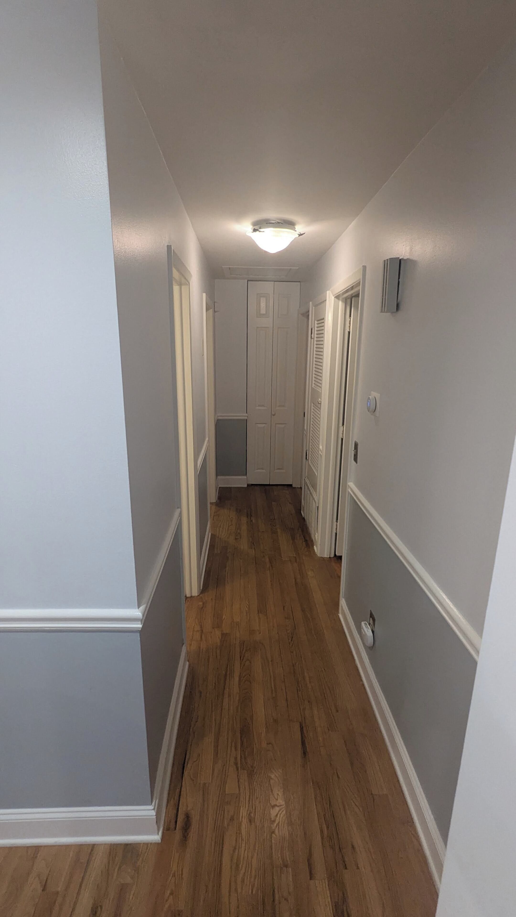 A hallway with wooden flooring, white walls, and a door at the end.