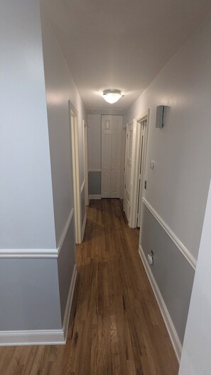 Un pasillo con suelo de madera, paredes blancas y una puerta al final.