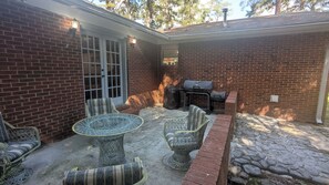 Un patio con pared de ladrillo, una parrilla cubierta y mobiliario de mimbre.