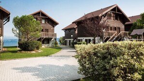 A row of wooden cabins with balconies, a paved walkway, and a view of the sea.