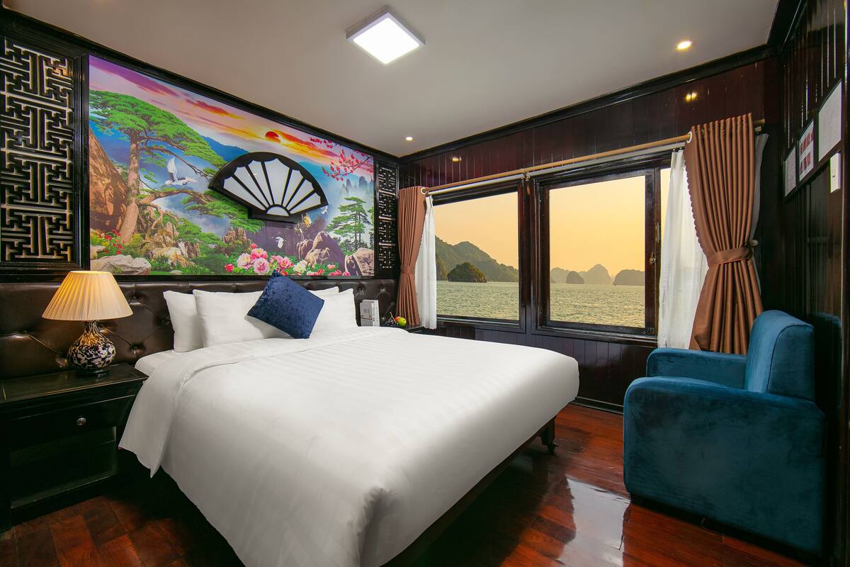 A hotel room with a large bed, a view of the sea through a window, and a decorative mural on the wall.