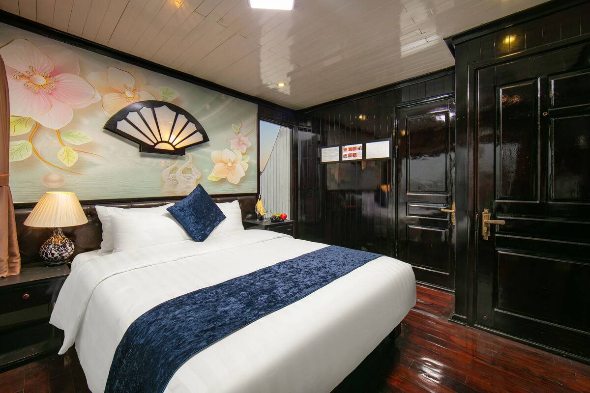 A hotel room with a large bed, a decorative wall with floral artwork, a traditional fan, and a black door with a sign.