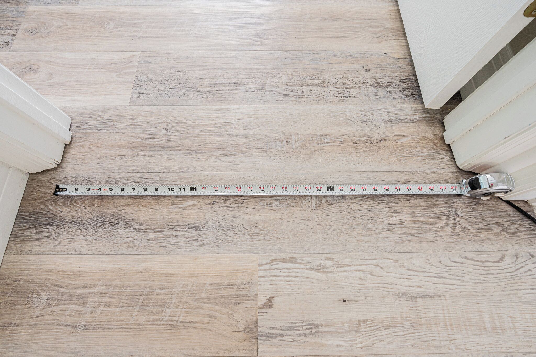 Un piso de madera con una cinta métrica extendida, mostrando las dimensiones de la habitación.