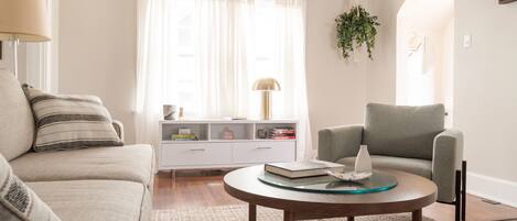 A living room with a sofa, armchair, coffee table, and a white console table with books and decorative items.
