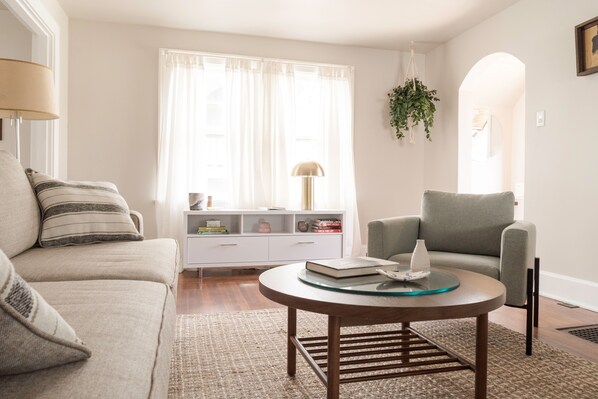 A living room with a sofa, armchair, coffee table, and a white console table with books and decorative items.
