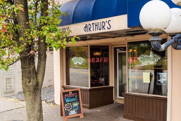 Experience a classic, inviting atmosphere at Arthur's Cafe, where a welcoming chalkboard sign and outdoor seating area invite you to dine in.
