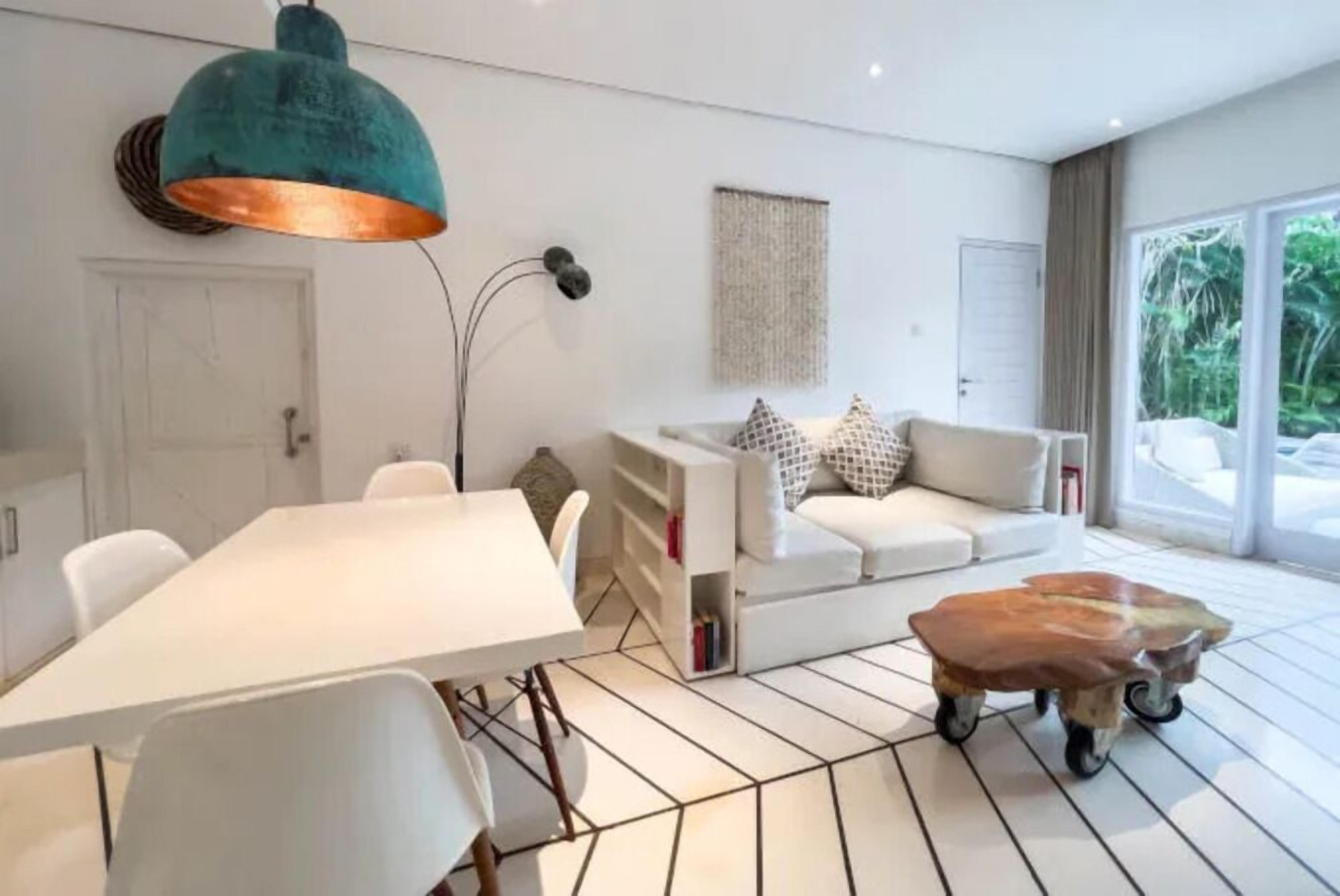 A modern living room with a white sofa, a white dining table, and a unique wooden coffee table.