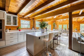 Een moderne keuken met houten balken, een groot eiland, barkrukken en een zithoek met een bank en tafel.