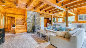 A log cabin interior with a stone wall, wooden floors, a fireplace, a sofa, and a kitchen area. - Luxurious & Enchanting Log House in Heart of Hudson Valley/Catskills, Upstate NY (Saugerties)