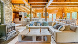 A cozy cabin interior with a stone wall, wooden beams, a sofa, a coffee table, and a kitchen area. - Luxurious & Enchanting Log House in Heart of Hudson Valley/Catskills, Upstate NY (Saugerties)