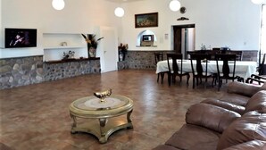 A spacious living room with a brown leather sofa, a round coffee table, and a dining area with a table and chairs. - Quinta Valvanera (Salta)