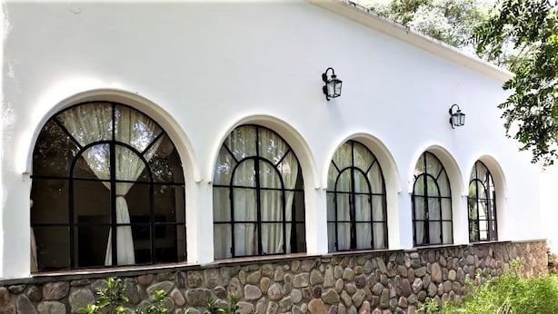 A building with a white exterior, stone base, and multiple arched windows with black frames. - Quinta Valvanera (Salta)