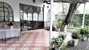 A covered patio area with a tiled floor, a table with a vase of flowers, and potted plants. - Quinta Valvanera (Salta)