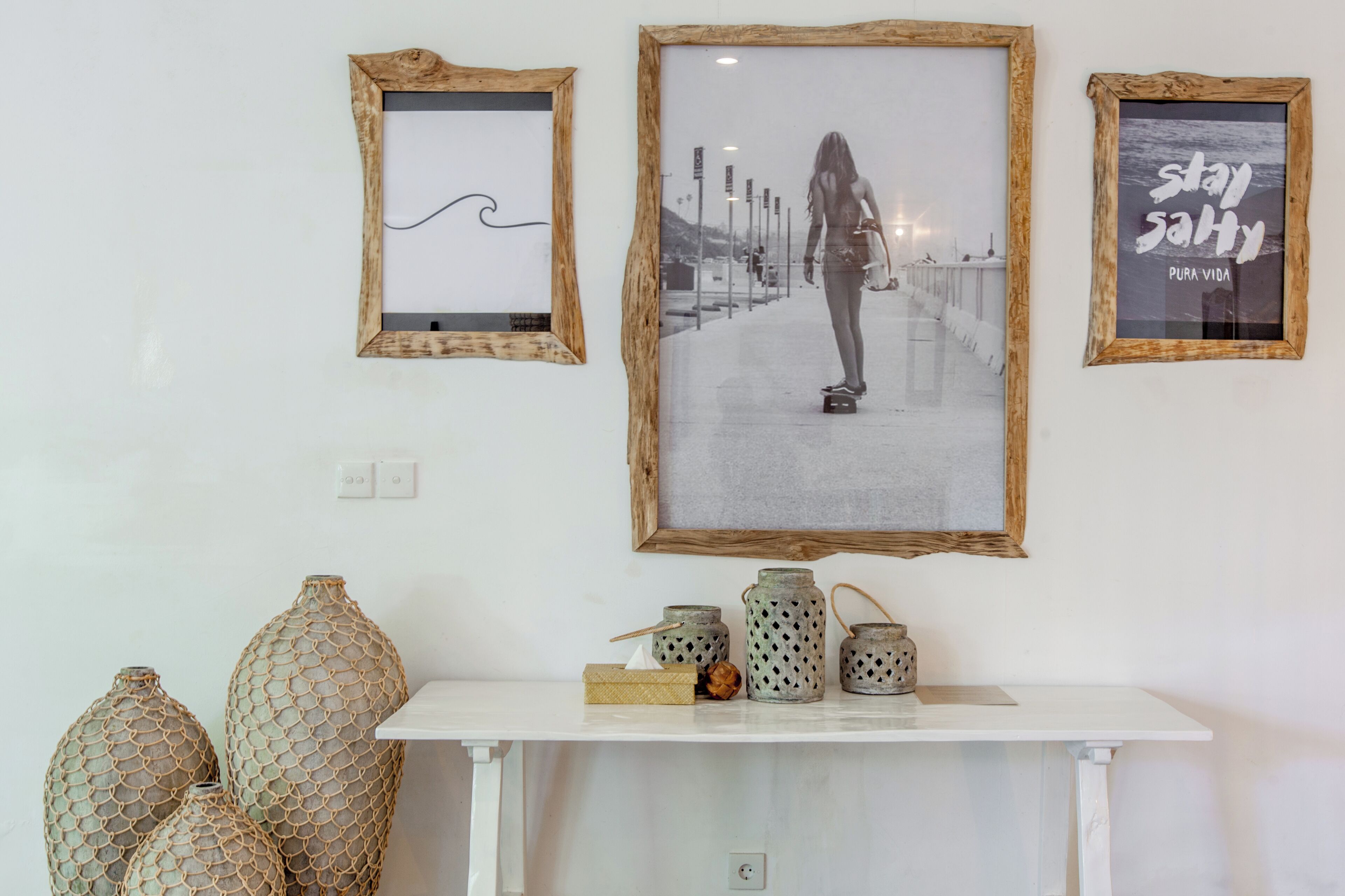 A wall with three framed pictures, a white console table with decorative jars, and a power outlet.