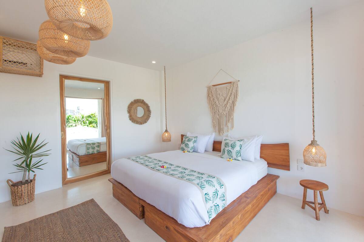 A bedroom with a wooden bed, a hanging macrame wall hanging, a wicker plant, and a woven light fixture.
