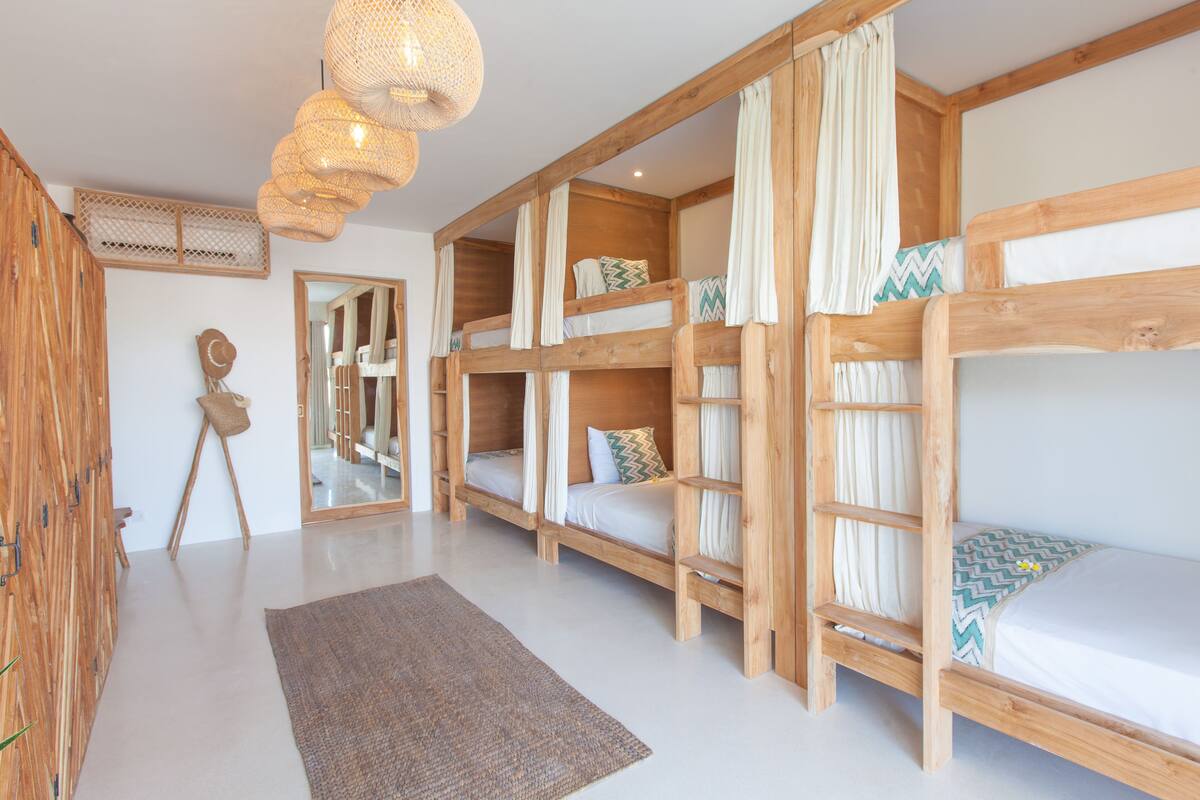 A room with bunk beds, a mirror, a woven light fixture, and a wooden wardrobe.