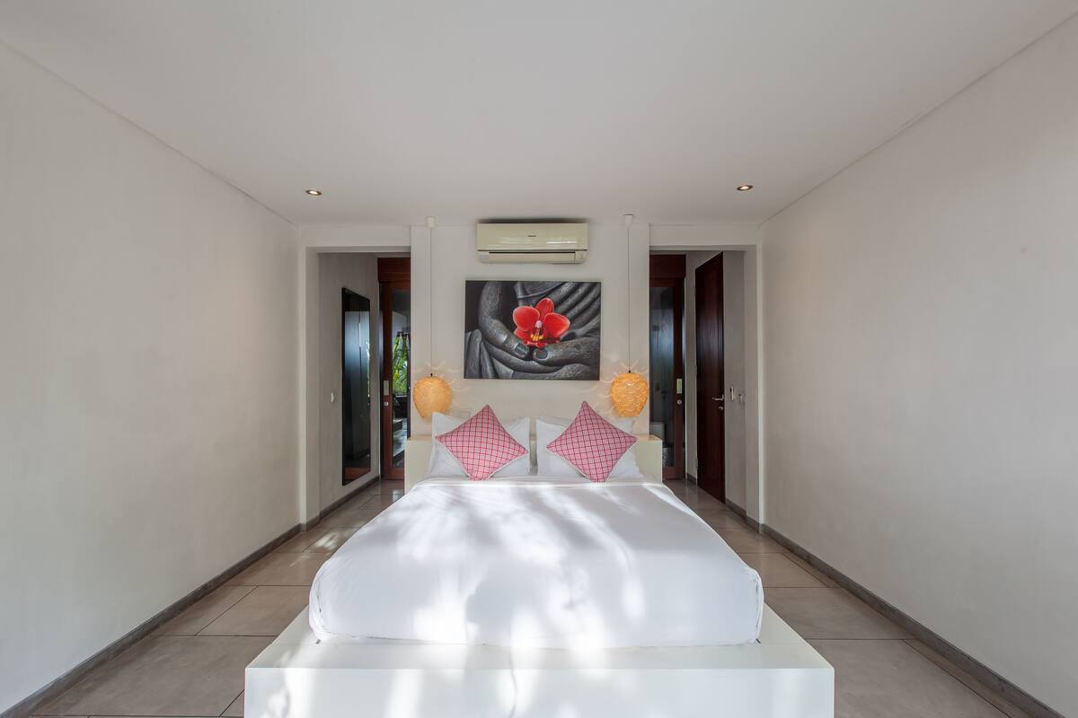 A spacious bedroom with a large bed, a central air conditioning unit, and a wall-mounted artwork.