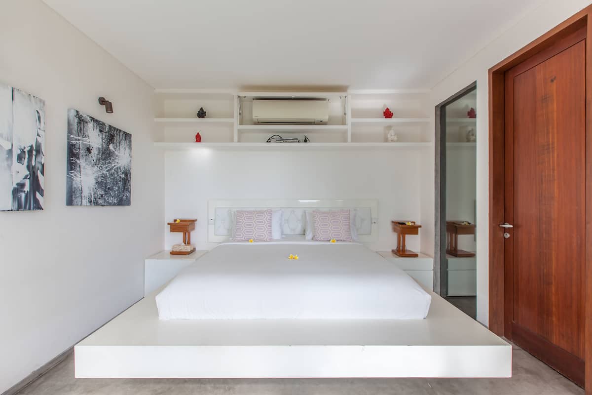 A modern bedroom with a large bed, built-in shelves, and a wooden door.