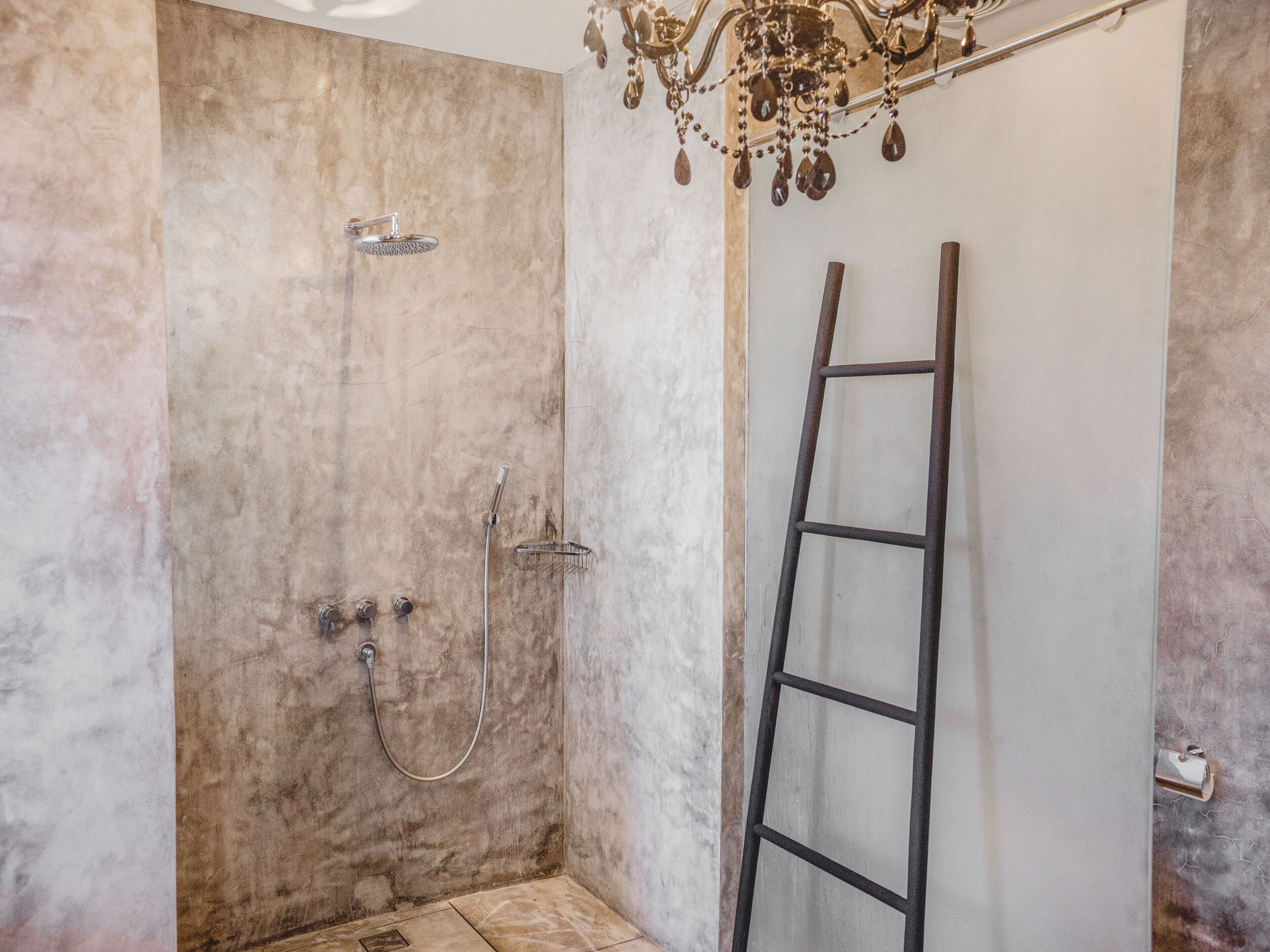 A shower with a marble wall, a showerhead, and a handheld shower attachment.