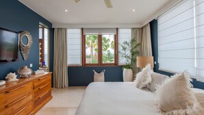 A bedroom with a large bed, a ceiling fan, a wooden dresser, and a TV on the wall. - AB Villa & Apartments (Seminyak)