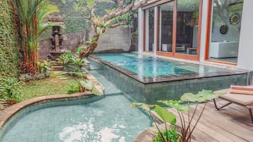 Relax by the serene pool surrounded by lush greenery and a modern building with a clean design.