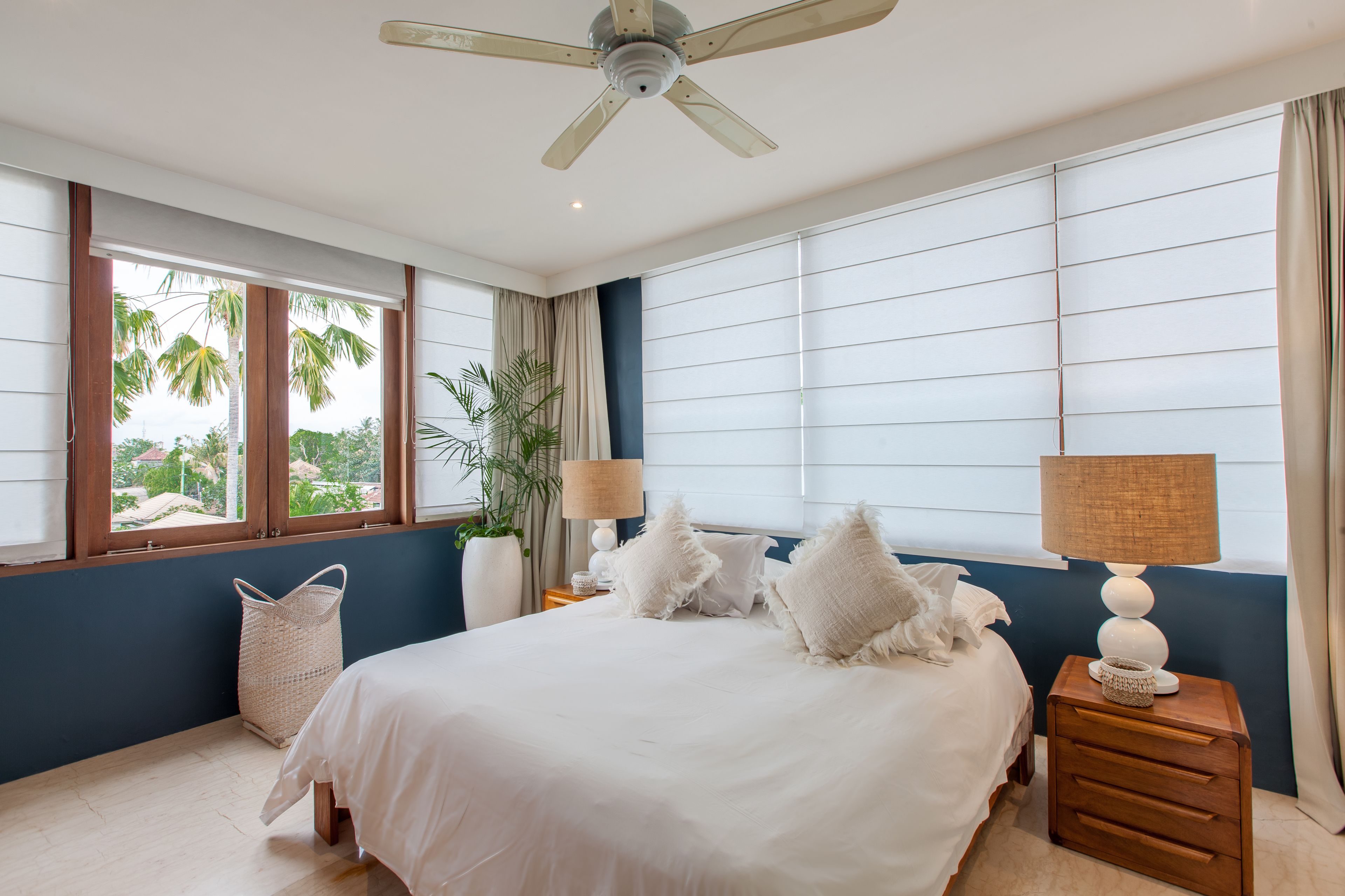A bedroom with a bed, nightstands, a ceiling fan, and large windows with curtains.