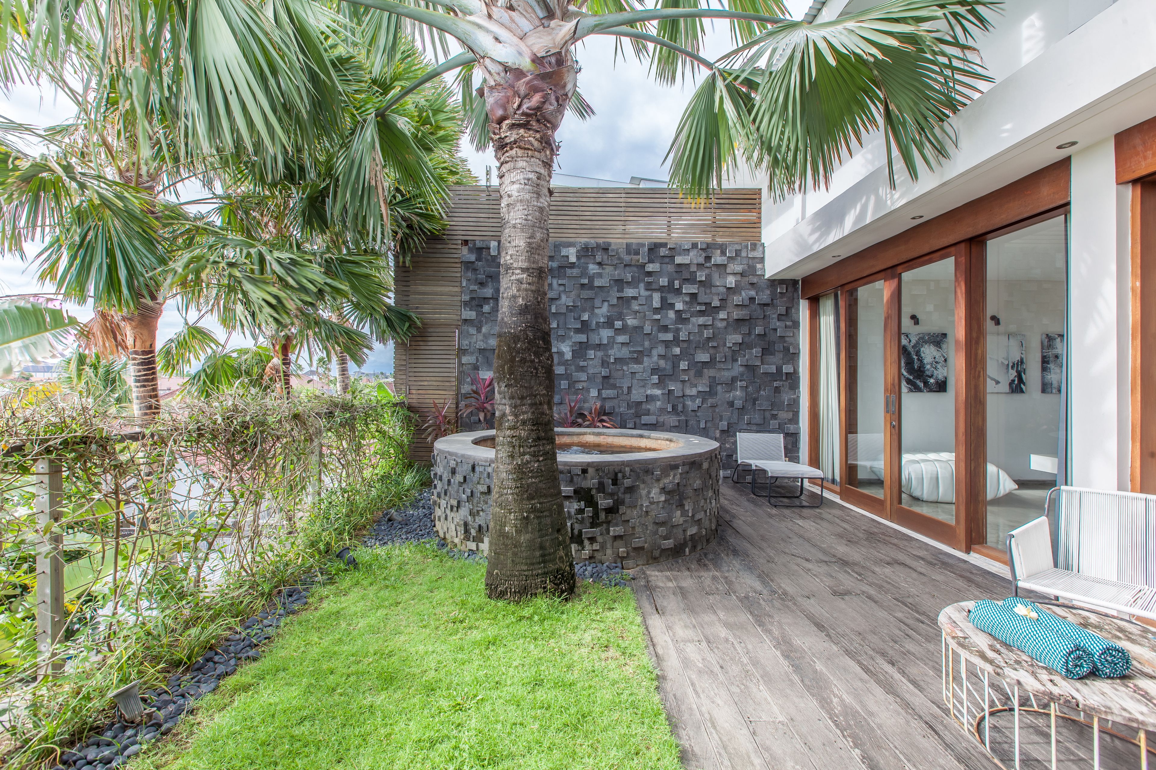 Un patio moderno al aire libre con un hogar a leña de piedra, una palmera y un área de estar con vista al océano.