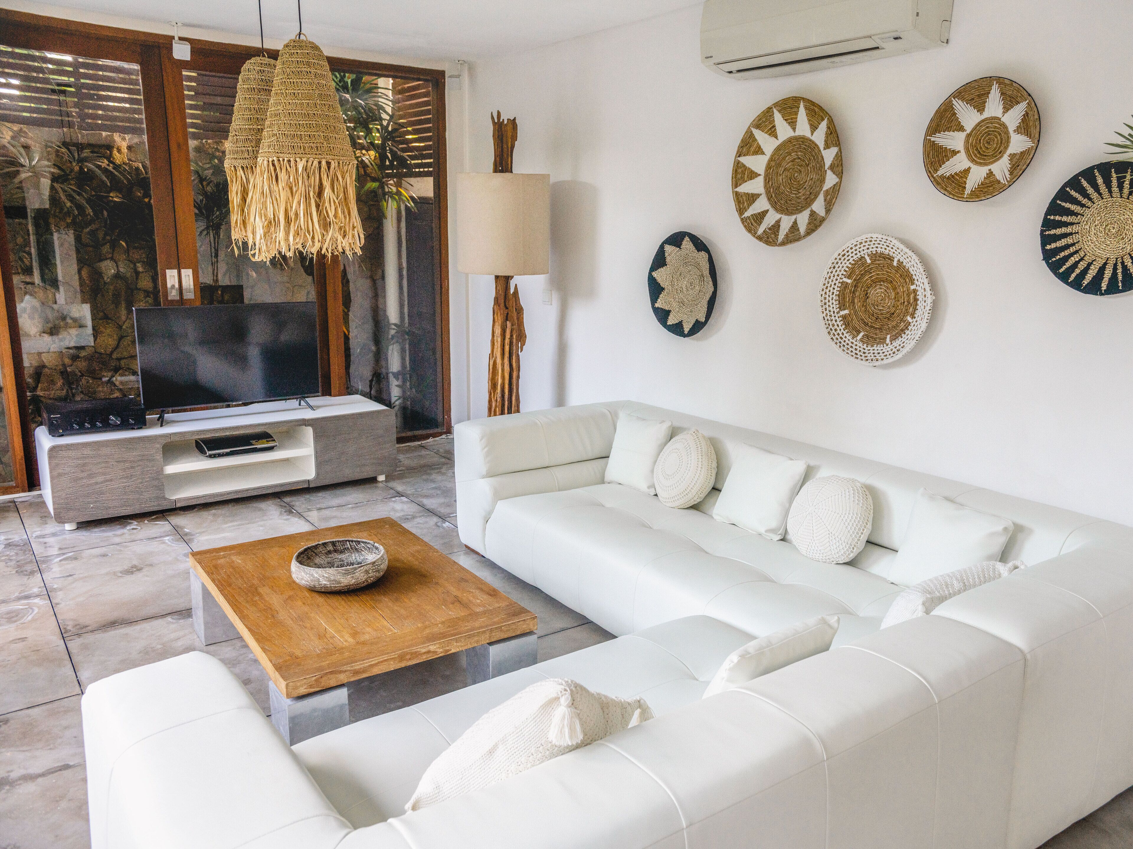 Una sala de estar moderna con un sofá blanco, una mesa de centro de madera y un televisor sobre un mueble gris.
