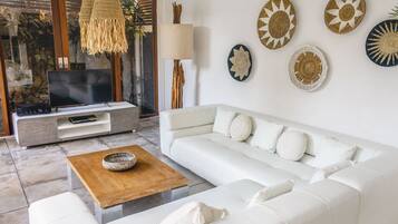 Una sala de estar moderna con un sofá blanco, una mesa de centro de madera y un televisor sobre un mueble gris.