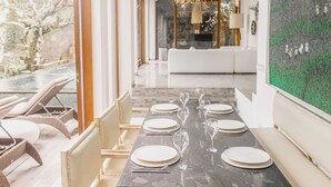 A modern dining area with a long table set for six, a white sofa in the background, and a large green textured wall. - AB Villa & Apartments (Seminyak)