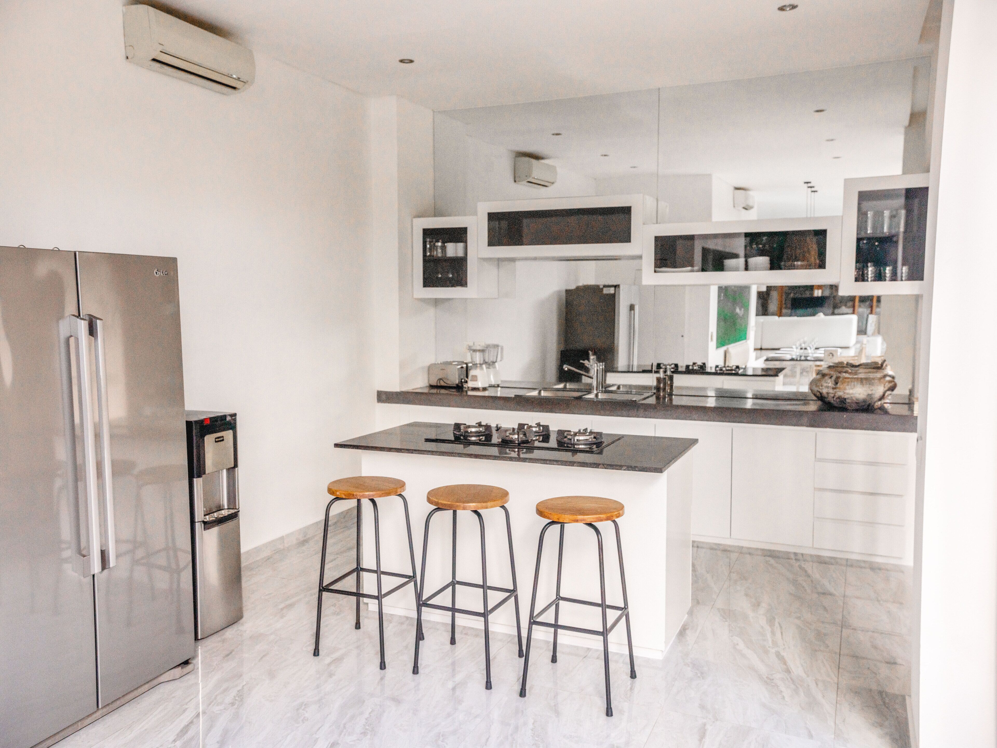 A modern kitchen with a stainless steel refrigerator, a central island with stools, and white cabinetry.