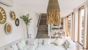 A modern living room with a white sectional sofa, a wooden coffee table, and a staircase leading to a kitchen. - AB Villa & Apartments (Seminyak)