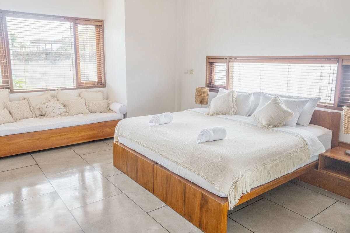 A bedroom with a wooden bed, white bedding, and a wooden bench with cushions.