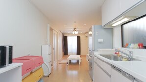A modern kitchen with white cabinets, a stainless steel sink, and a dining area with a table and chairs. - Hostel Tengachaya 238 (Osaka)