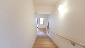 A narrow, wooden staircase with a handrail, leading to a room with a window and a ceiling-mounted light fixture. - Hostel Tengachaya 238 (Osaka)