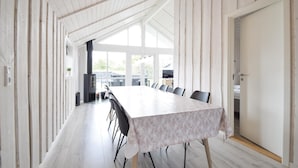 Una larga mesa de comedor con sillas, una estufa negra y vistas al exterior a través de amplios ventanales.