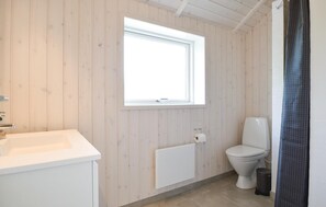 A bathroom with a wooden wall, a window, a toilet, a sink, and a radiator.