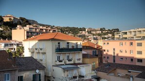 Ein mehrstöckiges Wohngebäude mit Balkonen, einer flachen Dachterrasse und einer Hanglage im Hintergrund.