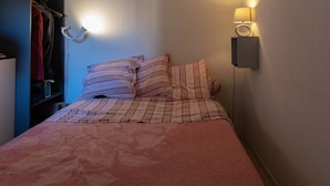 Ein Bett mit gestreifter Bettwäsche, eine Nachttischlampe und ein Kleiderschrank mit Kleidung.