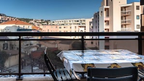 Ein Balkon mit Tisch und Stühlen, der auf einen Wohnbereich mit Gebäuden und einer Hügelkulisse blickt.
