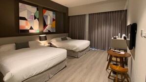 Ett hotellrum med två sängar, ett skrivbord med en stol, en TV och abstrakt konst på väggen.