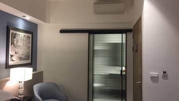 Een hotelkamer met een bed, een stoel, een bureau met een lamp, een ingelijst schilderij aan de muur, en een schuifdeur met ruitfolie.