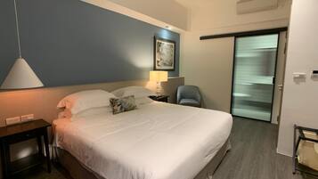 A hotel room with a large bed, a bedside table, a lamp, a chair, and a painting on the wall.