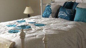 A neatly made bed with a white headboard and footboard, a lamp on a bedside table, and a wall with a textured artwork. - Beautiful lake view- (Lake Ozarks)