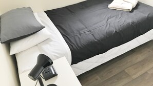 A neatly made bed with a black and white duvet, a grey pillow, and a folded white towel on the bed. There is a black lamp on a white bedside table. - Geraldine Heritage Hotel (Geraldine)