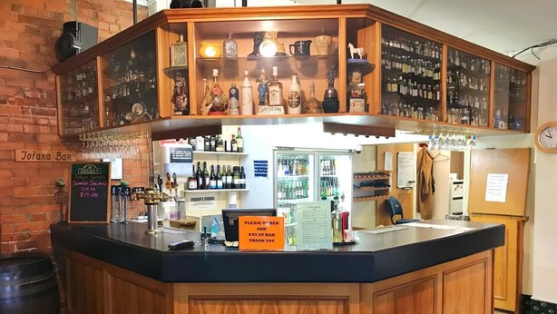 A bar area with a wooden counter, a cash register, and a menu board. - Geraldine Heritage Hotel (Geraldine)