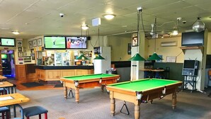 A billiards room with two pool tables, a bar area, and multiple screens displaying sports. - Geraldine Heritage Hotel (Geraldine)