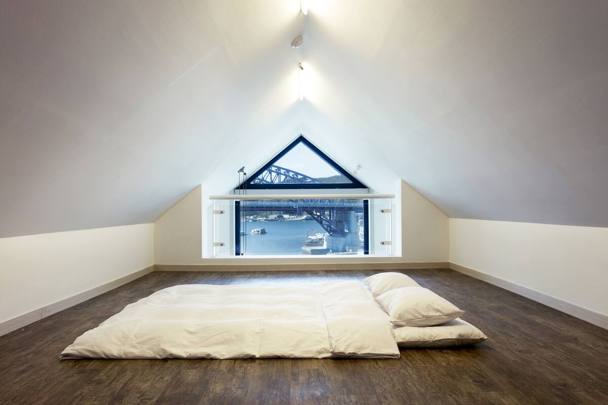 A spacious attic bedroom with a large window offering a view of a bridge and water.