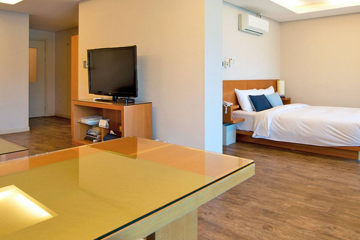 A hotel room with a bed, a TV on a stand, a bedside table, and a wooden floor.